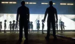 Siluetas de dos personas ante pequeños seres frente a una nave iluminada, en un fotograma de cine.
